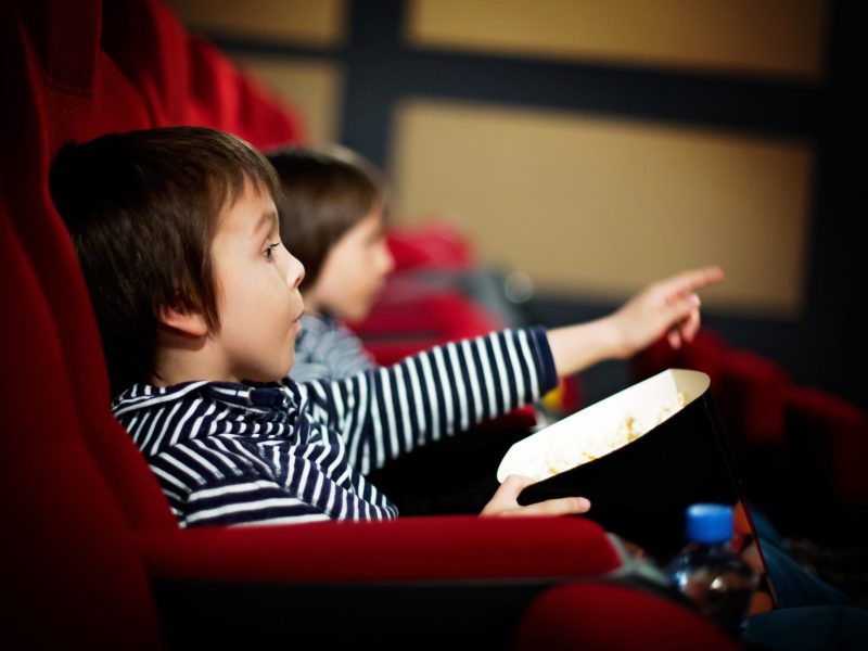 Two preschool children, twin brothers, watching movie in the cinema, eating popcorn