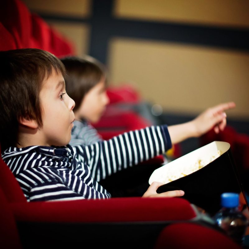 Two preschool children, twin brothers, watching movie in the cin Two preschool children, twin brothers, watching movie in the cinema, eating popcorn