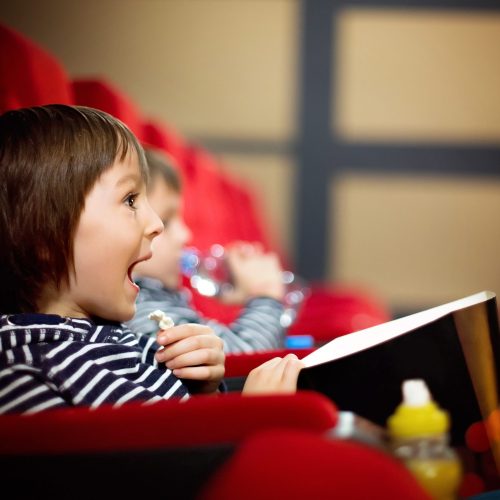 Two preschool children, twin brothers, watching movie in the cin Two preschool children, twin brothers, watching movie in the cinema, eating popcorn