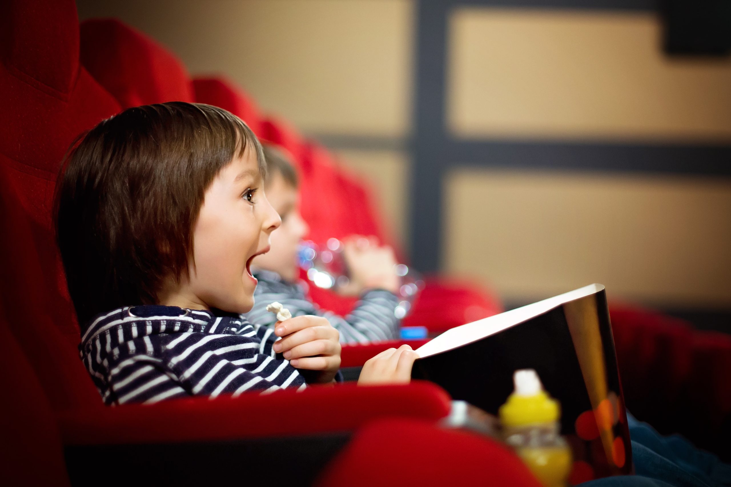 Two preschool children, twin brothers, watching movie in the cin Two preschool children, twin brothers, watching movie in the cinema, eating popcorn